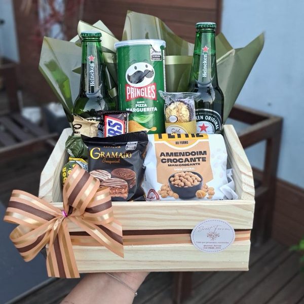 Cesta masculina em caixote de madeira com duas cervejas Heineken, batata Pringles, alfajor, amendoim e chocolates, com laço marrom.
