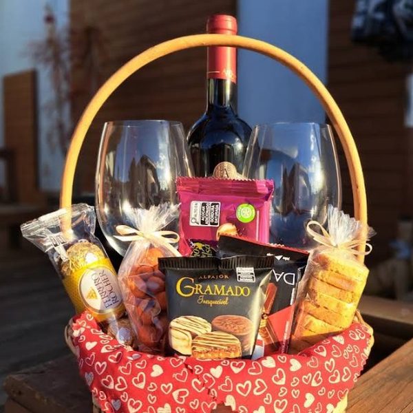 Cesta de presente com vinho, duas taças, alfajores, biscoitos amanteigados e castanhas, forrada com tecido de corações.